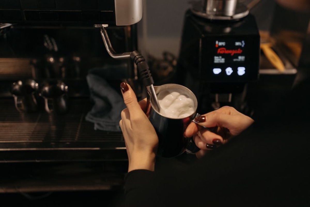 Steam wand frothing milk in a pitcher for espresso drinks at home